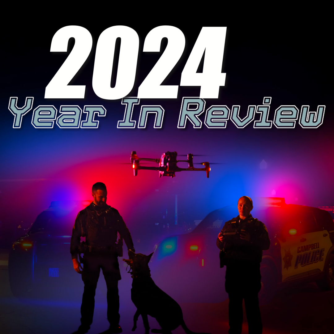 2 police officers in front of a police car with red and blue lights