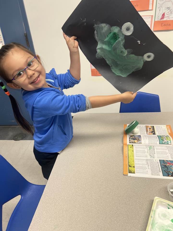pre-school student showing her painting of a frog